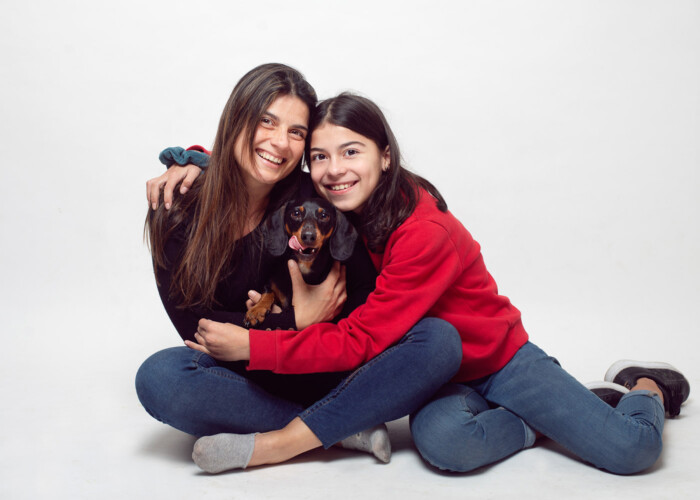 Dos mujeres abrazadas con un perro pequeño en estudio